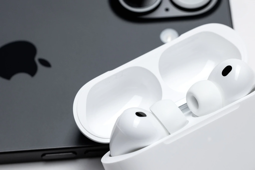 AirPods Pro 2026 posés sur une table, boîtier ouvert, avec un smartphone affichant une interface IA