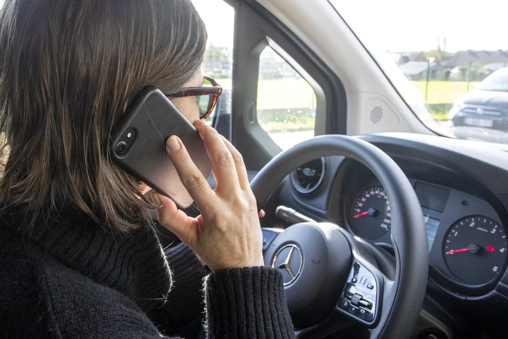 Conducteur tenant un smartphone avec GPS au volant, tableau de bord visible, rappel du permis suspendu