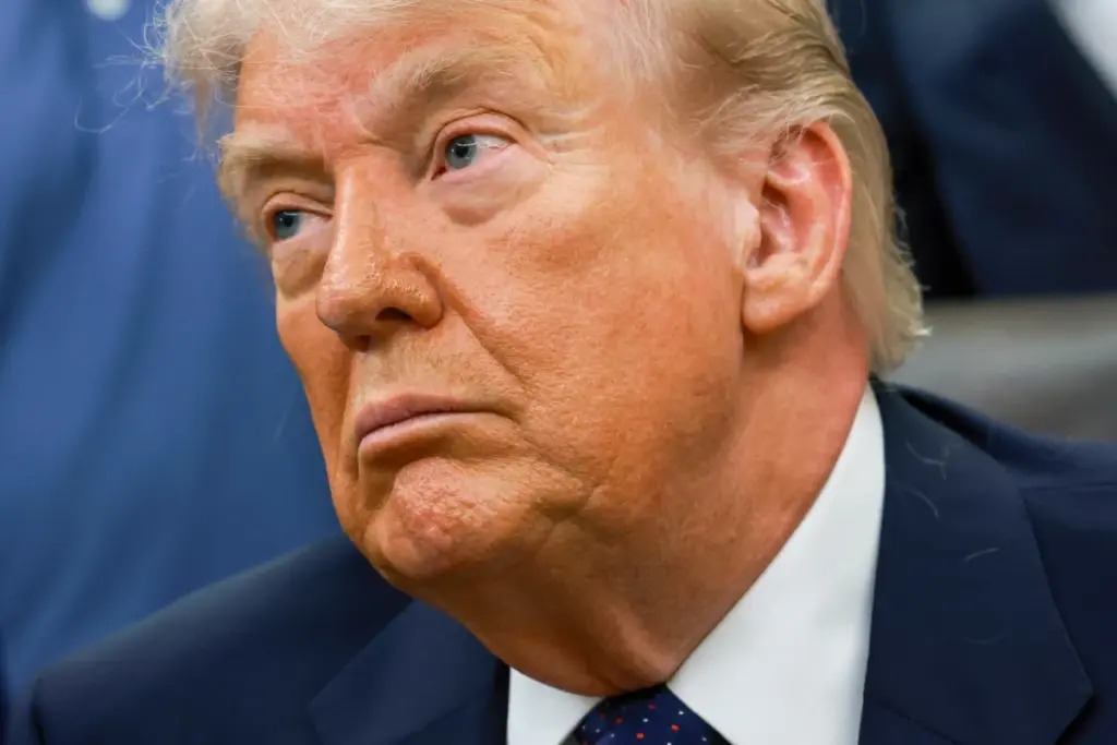 Donald Trump parlant à des journalistes devant des drapeaux américains, micro et pupitre au premier plan