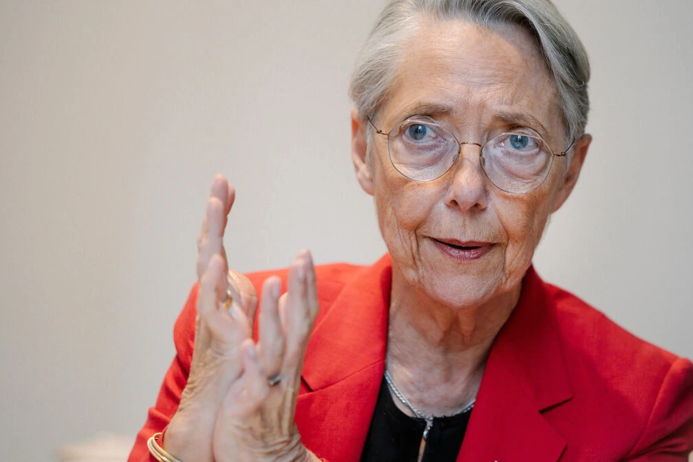 Élisabeth Borne debout devant des micros, regard sérieux, lors d’une prise de parole publique.