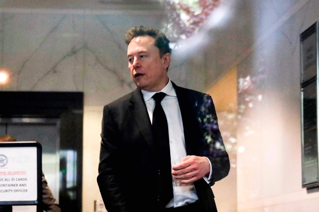 Elon Musk sur scène devant un écran géant affichant un schéma de puces IA et des graphiques techniques