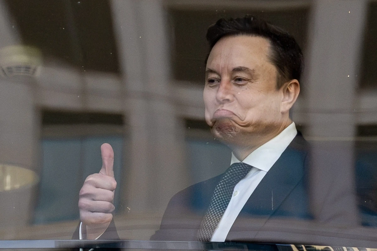 Elon Musk sur scène lors d’une conférence, micro à la main, devant un écran affichant « Claude ».