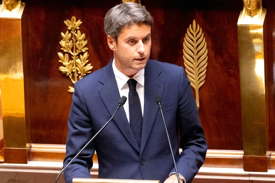 Gabriel Attal au pupitre, en costume, devant des élus locaux assis, lors d’une réunion publique