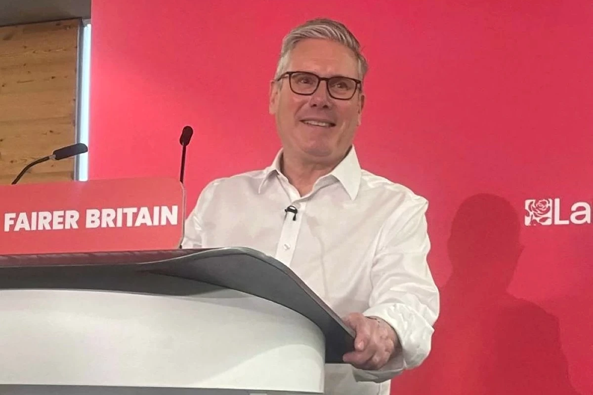 Keir Starmer devant un pupitre, micro et drapeaux britanniques en arrière-plan, regard sérieux