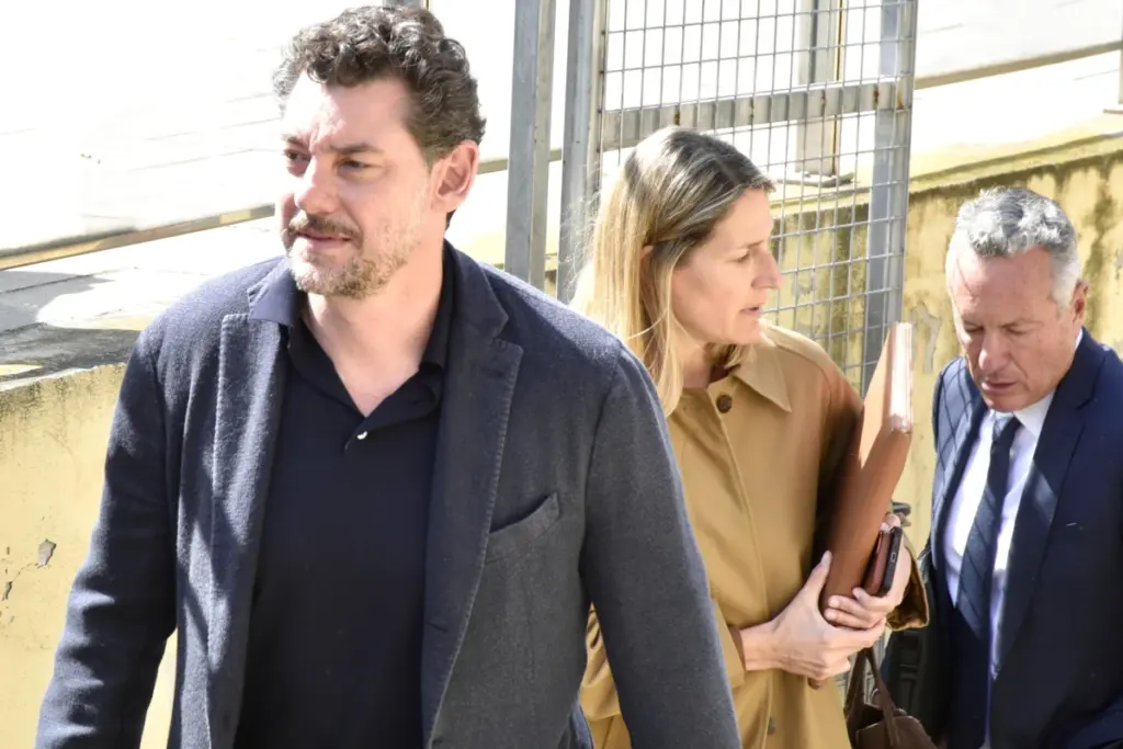 Le fils du fondateur de Mango escorté par la police devant un bâtiment, menottes aux poignets