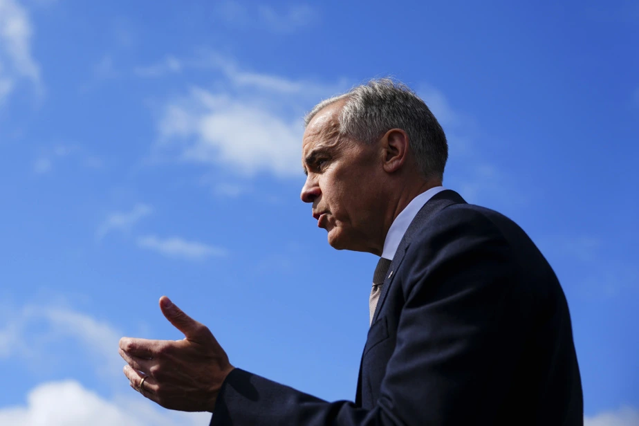 Mark Carney au pupitre lors d’une conférence de presse, drapeaux canadiens en arrière-plan