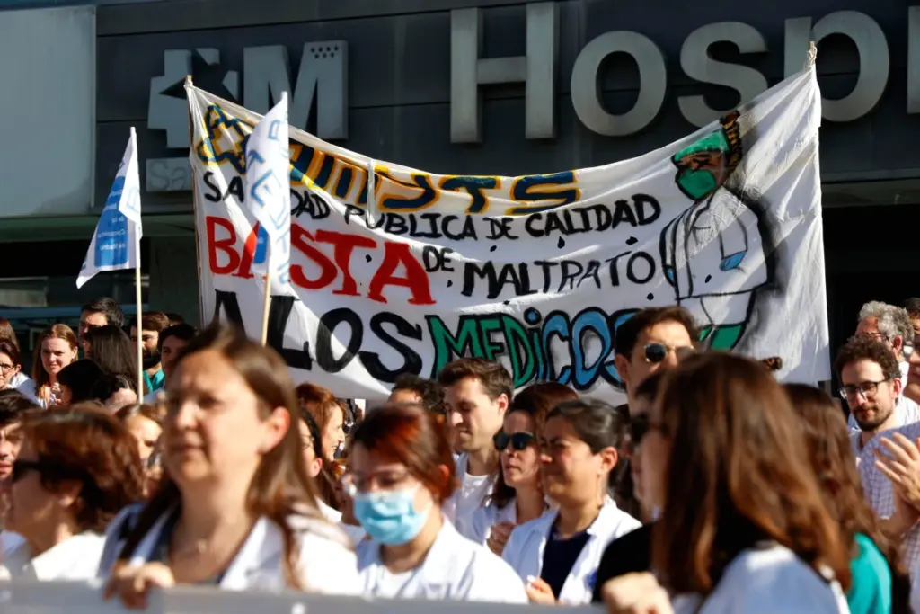 Médecins en grève devant un hôpital, blouses blanches et pancartes, petit groupe rassemblé