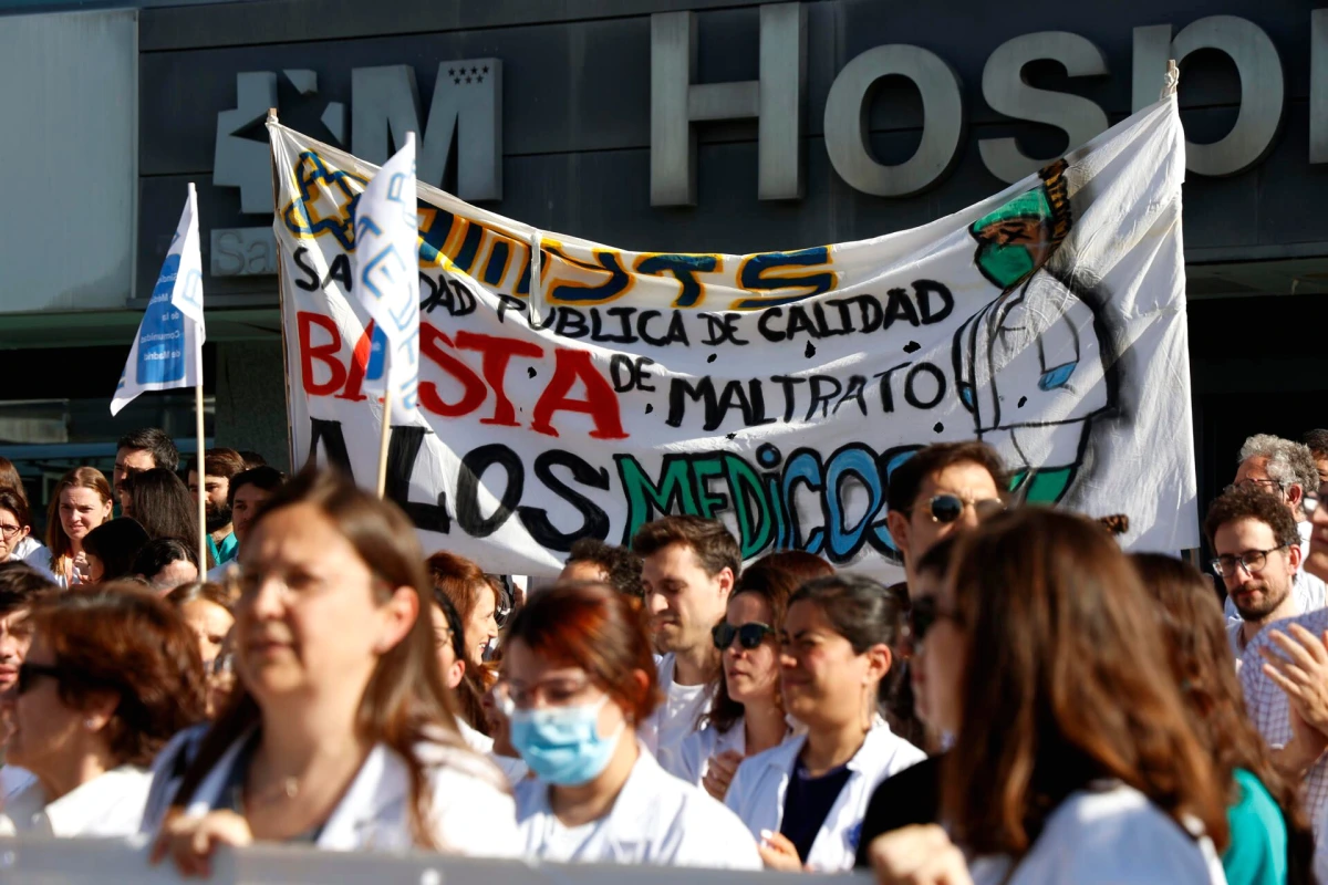 Médecins en grève devant un hôpital, blouses blanches et pancartes, petit groupe rassemblé