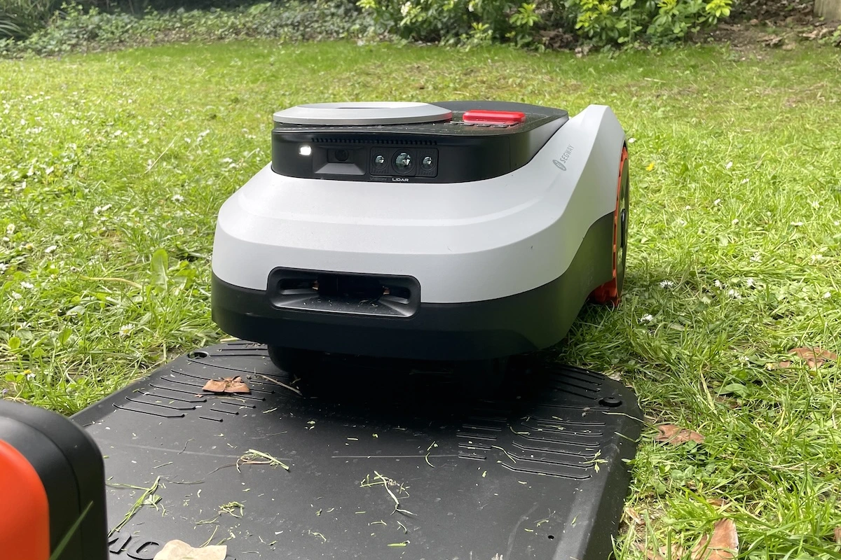 Robot tondeuse Segway Navimow i208 LiDAR sur une pelouse, avec sa base de recharge en arrière-plan