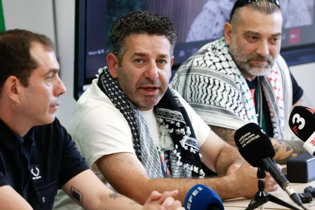 Saif Abukeshek en portrait, visage sérieux, devant un fond neutre avec un drapeau américain flou.