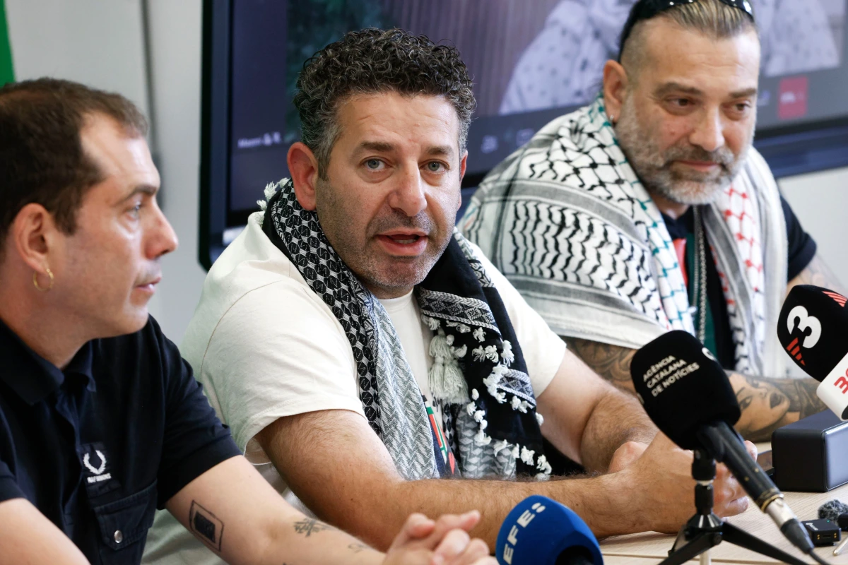 Saif Abukeshek en portrait, visage sérieux, devant un fond neutre avec un drapeau américain flou.