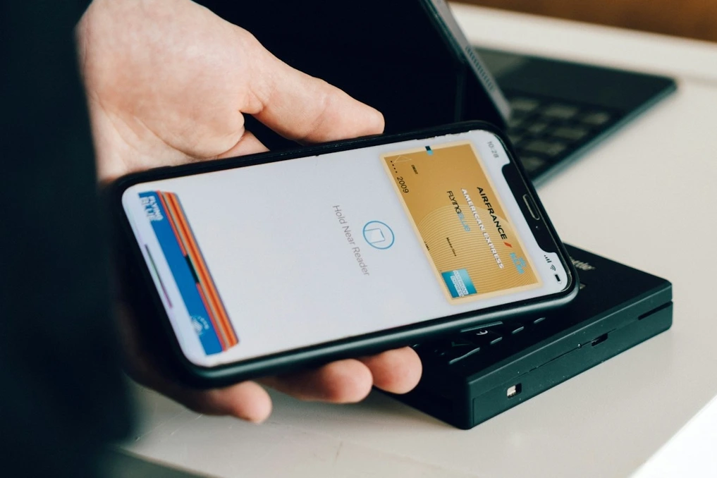 Smartphone affichant Apple Pay et Google Wallet, avec un écran de réglages de sécurité en arrière-plan
