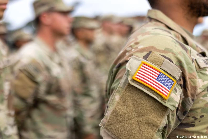 Soldats américains devant une base militaire en Allemagne, avec véhicules et drapeaux américain et allemand visibles