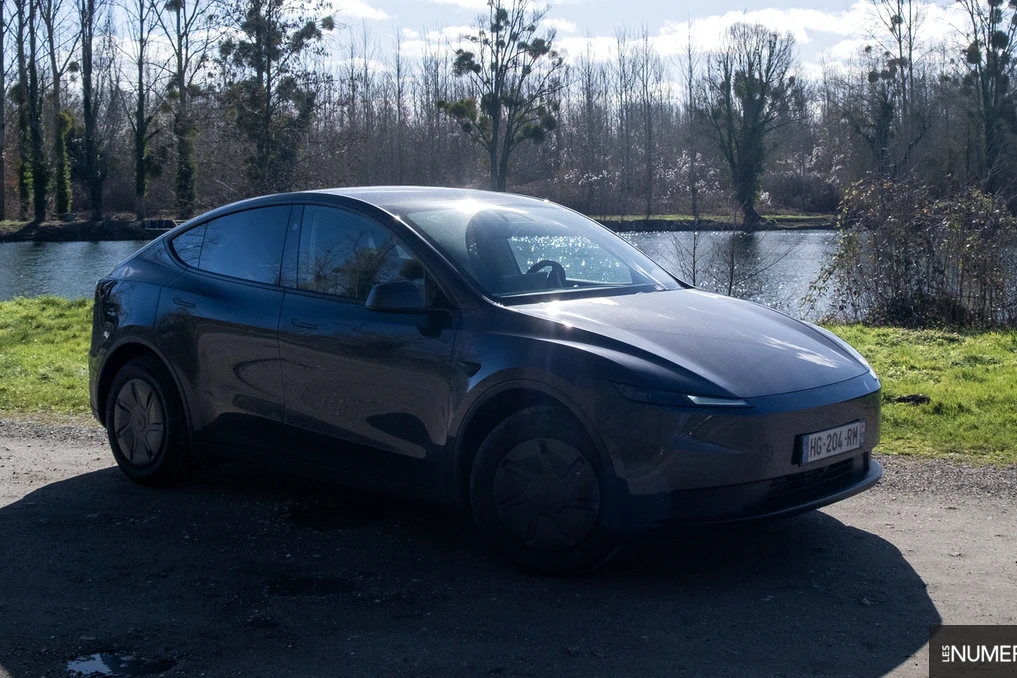 Tesla Model Y blanche sur route urbaine, écran central affichant l’Autopilot et icônes de conduite autonome