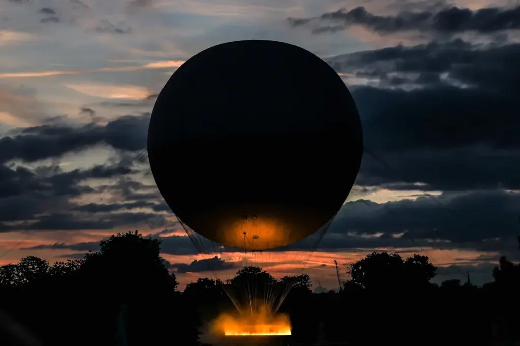 Vasque olympique illuminée la nuit à Paris, flamme dorée au-dessus d’une foule et de monuments en arrière-plan