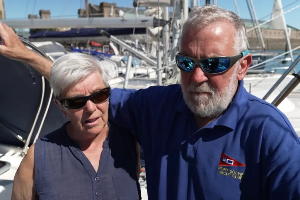 Couple britannique sur le pont d’un voilier, mer agitée, navire russe visible au loin dans la Manche