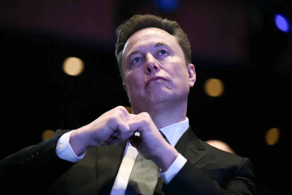 Elon Musk sur scène, micro en main, devant un écran lumineux lors d’une conférence technologique