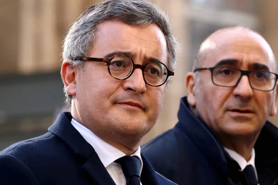 Gérald Darmanin en costume, parlant à des journalistes devant un bâtiment officiel, micros tendus.