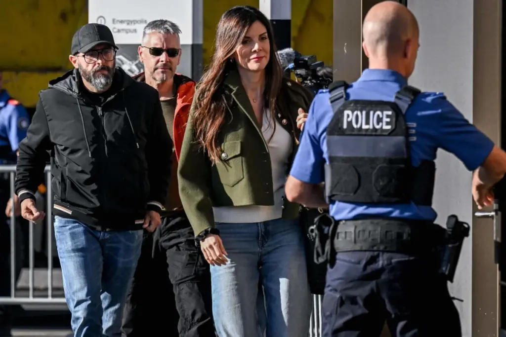 Jessica Moretti devant un bâtiment incendié à Crans-Montana, avec ruban de police et pompiers en arrière-plan