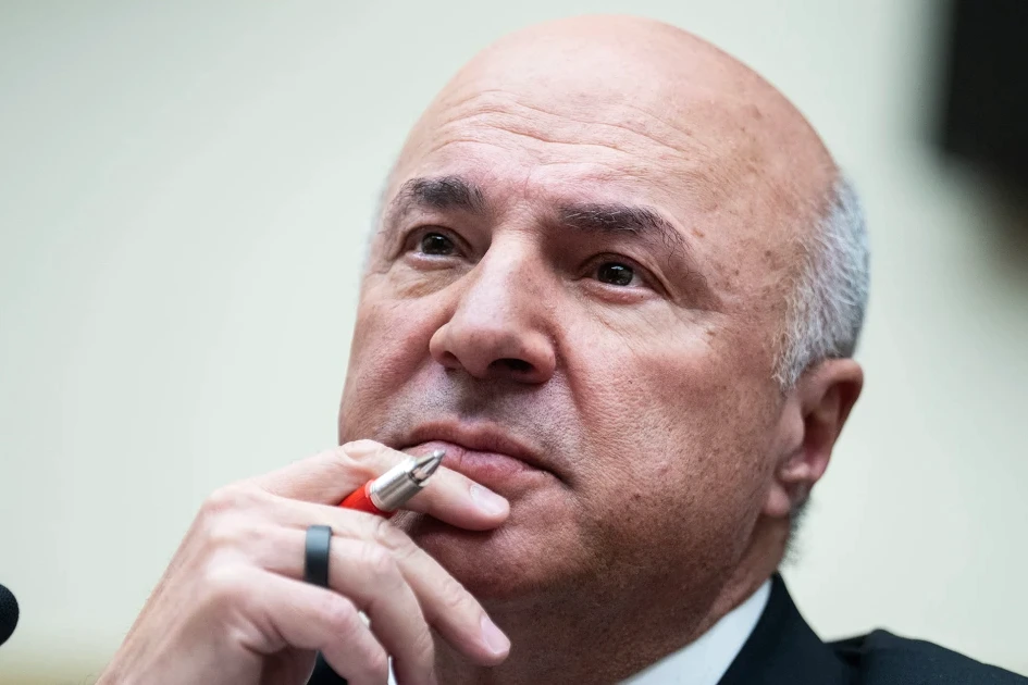 Kevin O’Leary en costume devant un data center, avec rangées de serveurs et câbles en arrière-plan
