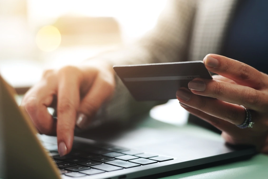 Main tenant une carte bancaire devant un ordinateur portable affichant une page de paiement en ligne
