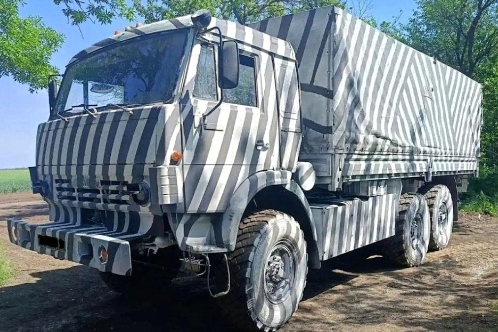 Véhicule de l’armée russe peint en camouflage zèbre noir et blanc, stationné sur une route boueuse.